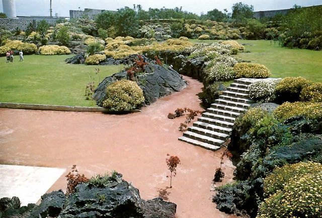 Panoramic view of a scenic natural landmark featuring unique rock formations, lush vegetation, and a winding path.